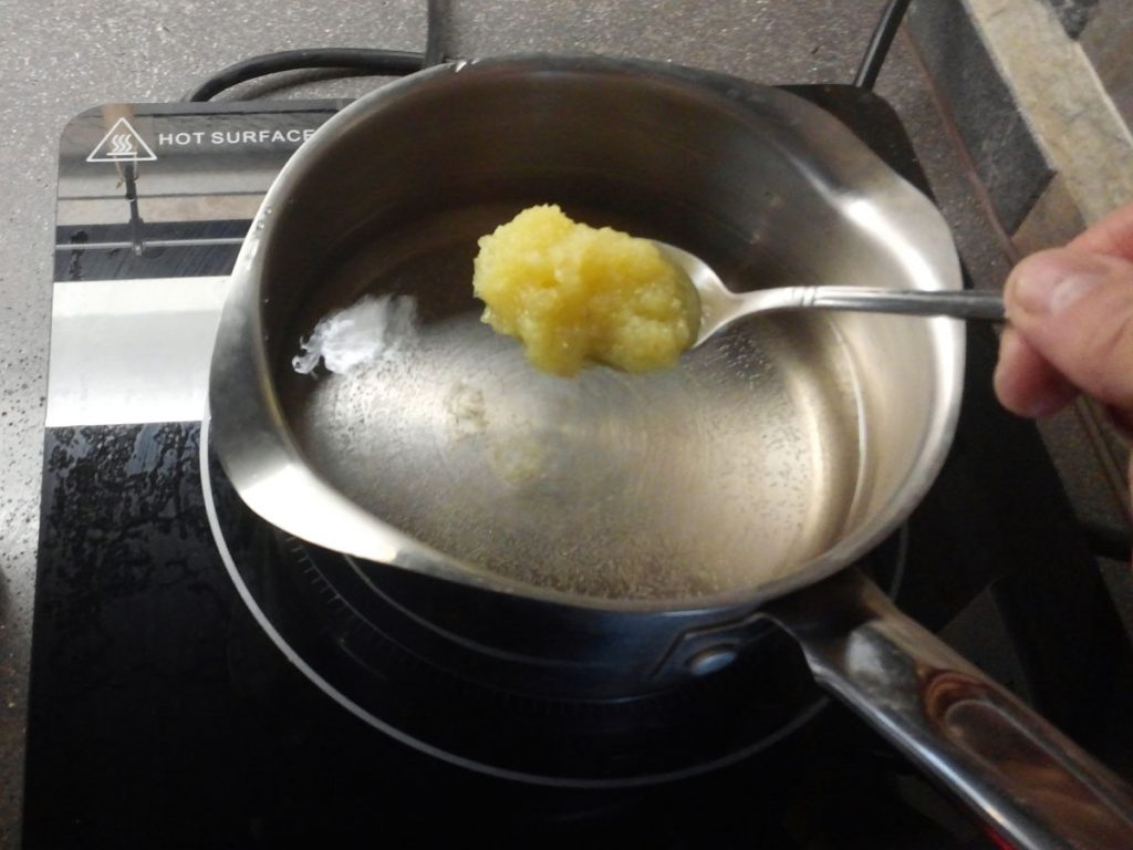 A spoon of ginger-sugar mixture is added to a pot of boiling water.