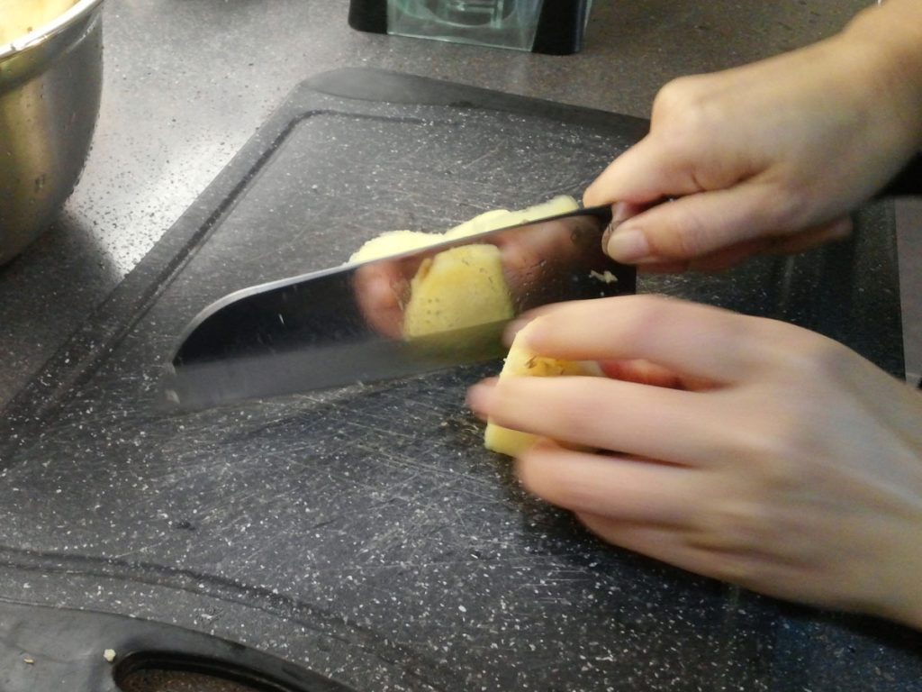 A piece of peeled, fresh ginger is being chopped on a cutting board. 