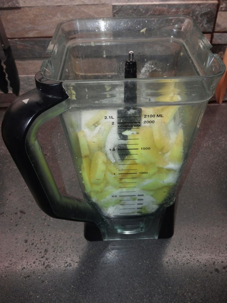 A blender contains a mix of sugar and chopped pieces of peeled ginger. 