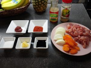 Ingredients are laid out in small square bowls and on a dish. In the square bowls on the left: hot pepper paste, hot pepper flakes, sugar, minced garlic, soy sauce. In bottles above: sesame oil, sesame seeds. On a ceramic plate on the right: chopped onions, chopped carrots, chopped pork.