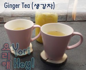 Ginger Tea recipe. Image of two pink-colored cups of tea on a kitchen countertop. Behind is a mason jar full of a yellowish, blended mixture of ginger and sugar.
