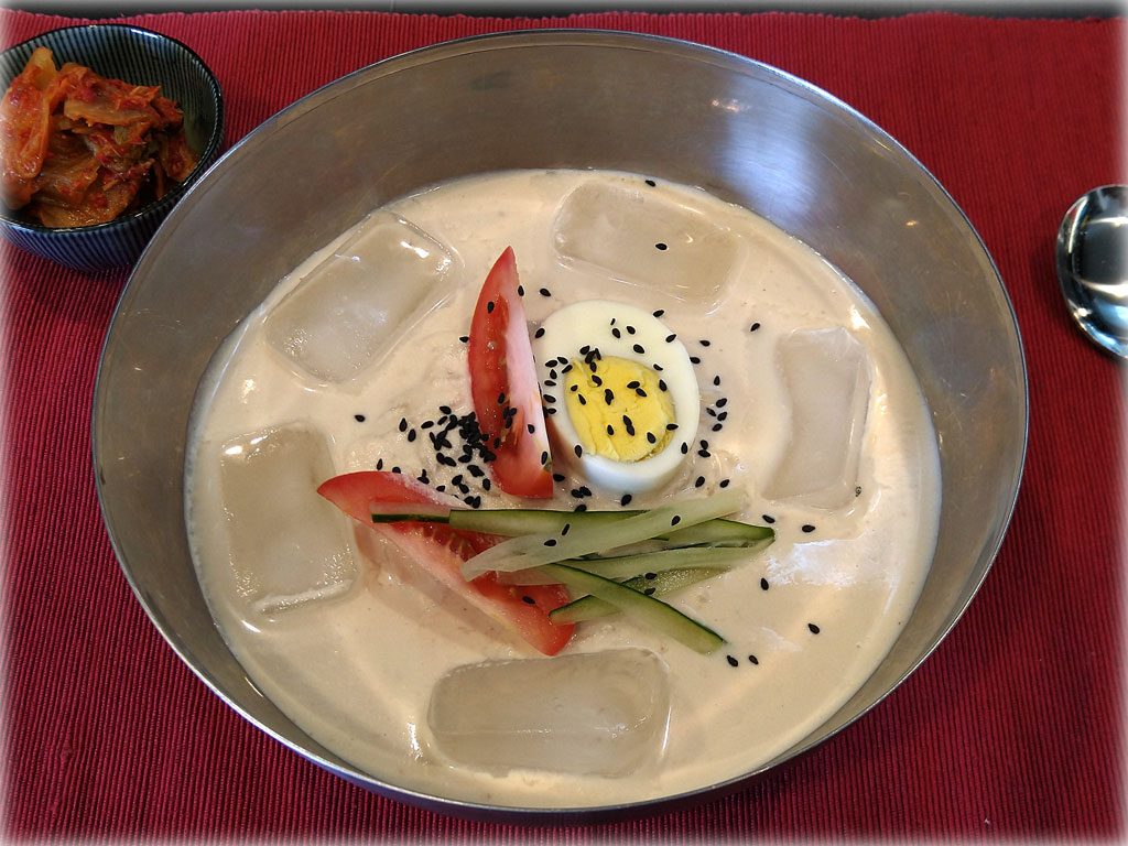 KongGukSu (콩국수) - Korean Cold Noodles in Soy Bean Broth - Dish served with cucumber, tomato and sesame seeds for garnish with ice cubes in broth